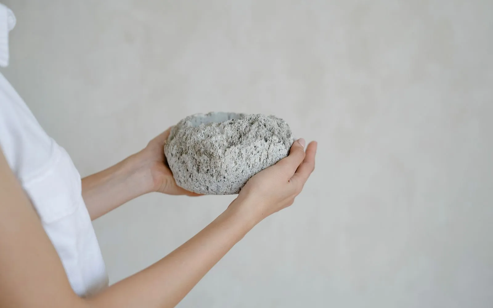 Bàn tay nâng viên đá xám thô trên nền sáng